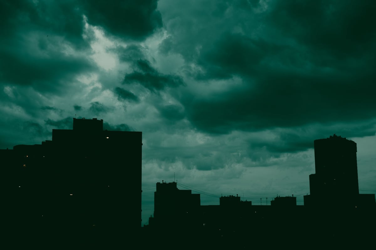 A dramatic cityscape at night features silhouettes of the buildings against moody sky with dark low clouds